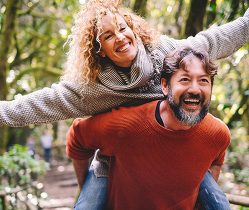 Smiling man in red-orange sweater giving piggy back ride to woman with curly hair