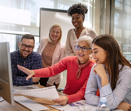 Woman in coral sweater discussing work projects with people around a computer