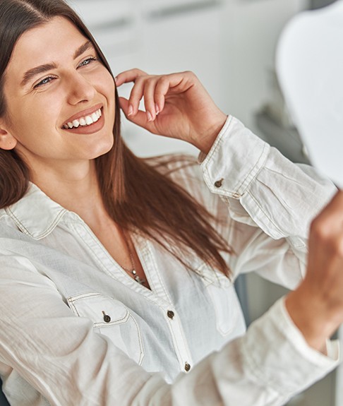 A woman admiring her treated teeth with a hand mirror