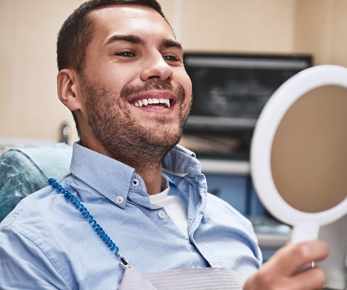 Man at dentist’s office checking smile in mirror
