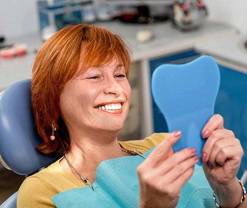 A woman using a hand mirror to admire her new dentures