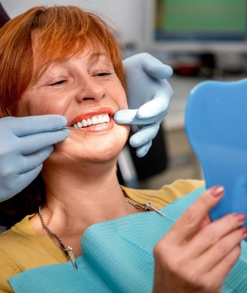 Woman looking at smile after dental implant tooth replacement