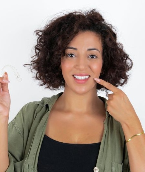 Smiling woman holding Invisalign aligner and pointing at her teeth