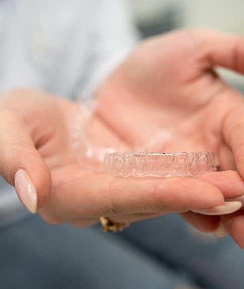 Manicured hands holding Invisalign clear aligners