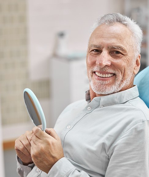 Male dental patient checking smile in mirror after teeth whitening in Lakewood, CO